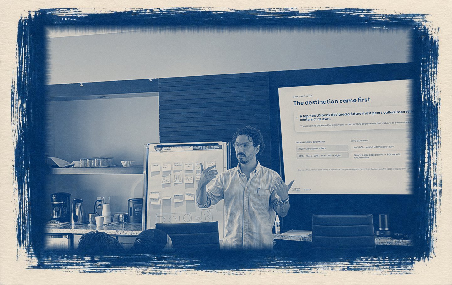 A cyanotype print of a workshop: a facilitator talks the room through a case study, with a board of sticky notes beside him and a slide on the screen behind.